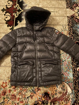 Svart dunjacka Parajumpers Sheen - Säljer en svart Parajumpers Sheen dunjacka med huva och coolt PJS-märke på ärmen. Den är storlek Y-S som motsvarar XS eller 164. Den har en liten skada som syns endast om man söker efter den, inget som syns tydligt. Den är annars en stabil 9/10 skick. Om du har frågor eller ngt bara komma in var ej blyg😊