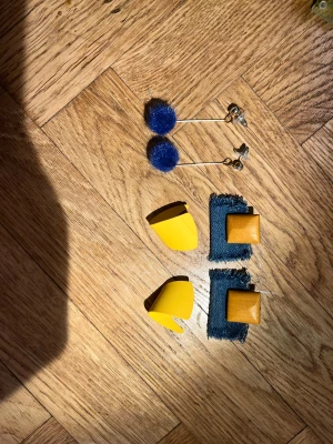 Tre par färgglada örhängen - Säljer tre par unika örhängen! Ett par med blå fluffiga bollar på silverfärgade stift, ett par med gul böjd plast i modern design och ett par med fyrkantiga trädetaljer på blå denimtyg. Perfekt för dig som gillar att sticka ut med accessoarer.