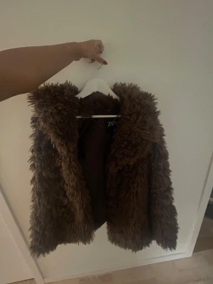 Brun pälsjacka från Zara, M - Säljer en fluffig brun pälsjacka från Zara i storlek M. Jackan har en cool oversized look med långhårig pälsimitation och är perfekt för dig som vill sticka ut. Fodrad insida och mjuk känsla, passar dig som gillar trendiga statement-plagg.