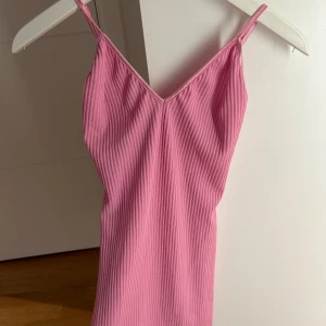 Rosa ribbad klänning från Chiquelle - Säljer en rosa ribbad klänning från Chiquelle i storlek M. Klänningen har smala axelband och v-ringning, vilket ger en enkel och stilren look. Perfekt för varma dagar och enkel att styla med accessoarer. Helt ny aldrig använd 