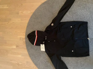 Svart Moncler Vindjacka - Svart Moncler Windbreaker. Storlek 1 (Motsvarar S). NFC scan fungerar. Tar ej emot byten och priset går tyvärr ej att diskuteras. Fråga gärna för fler bilder eller funderingar.