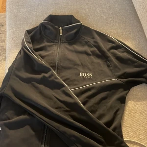Svart ziptröja från Hugo Boss - Svart ziptröja från Hugo Boss, skavanker finns, rödflammiga fläckar efter hårfärg på märket.