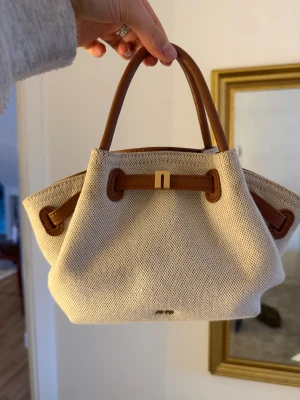 Beige handväska från JW PEI - Snygg beige handväska från JW PEI med bruna detaljer och handtag i skinn. Väskan har en stilren och modern form. Super fin och söt man kan antingen hålla den i handen, men även ett långt band ingår så du kan ha den crossbody