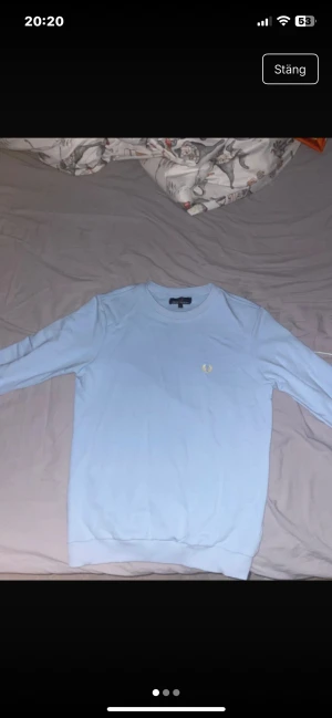 Ljusblå Fred Perry  - Snygg ljusblå tröja från Fred Perry i storlek S. Klassisk design med rund hals och det ikoniska Fred Perry-logot broderat i vitt på bröstet. Tillverkad i mjuk bomull och har långa ärmar med ribbade muddar för en clean look. Använd 1 gång 