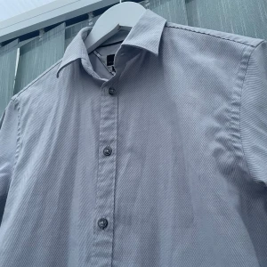 Skjorta från Zara - Snygg grå skjorta från Zara i slim fit-modell med diskret randigt mönster. Skjortan har klassisk krage, långa ärmar och knappar framtill. Perfekt för dig som gillar stilrena och moderna plagg med en clean vibe | Passar för 175-180 |