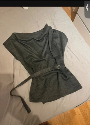 Mörkgrå omlottklänning med bälte - Snygg mörkgrå omlottklänning med bälte i midjan som ger en cool siluett. Klänningen har korta ärmar och är tillverkad i ett mjukt material som känns skönt mot huden. Perfekt för dig som gillar minimalistisk stil och vill ha något enkelt men ändå trendigt.