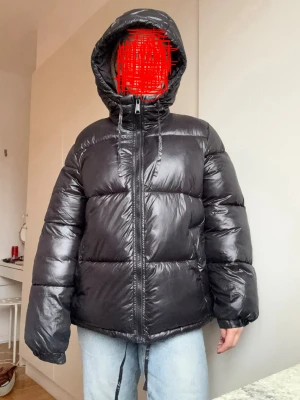 Svart pufferjacka med huva - Svart glansig pufferjacka. Varm ock skön för vintern.
