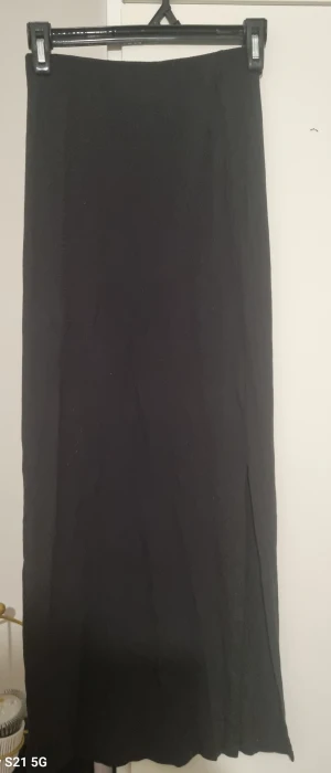 Svart långkjol med slits - En stilren svart långkjol med rak passform och diskret slits på sidan. Kjolen har en minimalistisk design och är perfekt för dig som gillar en clean och enkel look. Materialet känns mjukt och följsamt mot kroppen.