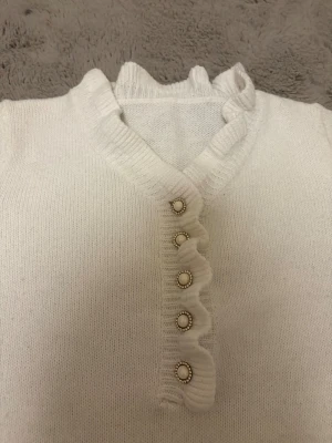 Vit stickad tröja med pärlknappar - Supersöt vit stickad tröja med volangkant vid halsen och längs knappraden. 