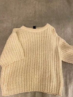 Beige/gul stickad tröja med kort ärm - Supermysig beige/gul stickad tröja med grov struktur och korta ärmar. Tröjan har en rund halsringning och ribbade muddar vid ärmslut och nederkant. Perfekt för lager-på-lager under hösten eller vintern. Snygg att styla med jeans eller kjol.