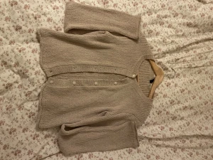 Beige stickad kofta från H&M - Mysig beige stickad kofta från H&M i storlek S. Koftan har ribbad struktur, rund hals och knappar framtill. Långärmad och med en lite croppad passform som ger en chill vibe. Perfekt att slänga på sig när det är lite kyligt ute.