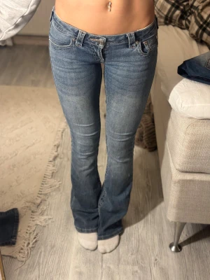 Bootcut jeans från True Religion - Snygga blå bootcut jeans från True Religion med låg midja och klassiska fickor med broderade detaljer. Jeansen har en lätt tvättad look och är gjorda i mjukt denim med stretch för skön passform. Perfekta för dig som gillar retrovibbar och markerad siluett.