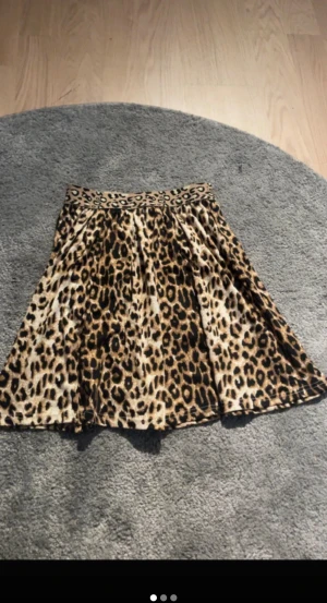 Leopardmönstrad kortkjol - Säljer en snygg kortkjol med leopardmönster i beige, brunt och svart. Kjolen har en utställd form och bred linning med samma mönster. Perfekt för dig som vill sticka ut med djurprint och cool stil.