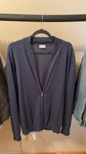 Marinblå kofta från John Henric - Snygg marinblå kofta från John Henric i 100% merinoull. Den har långärmad design, ribbad krage och muddar samt en stilren dragkedja framtill. Perfekt för dig som gillar klassisk stil med modern touch.