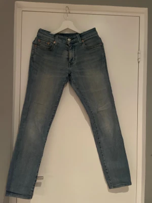 Levi's 551 ljusblå jeans W28 L32 - Säljer ett par Levi's 551 jeans i ljusblå tvätt med klassisk femficksdesign. Jeansen har raka ben och normal passform, med detaljer som nitar och Levi's patch bak i brunt läder. Perfekt för dig som gillar en chill och tidlös look.