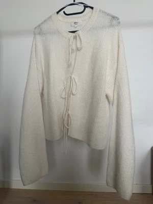 Stickad kofta Gina Tricot - Vit stickad kofta från Gina Tricot i storlek L. Koftan har ribbad struktur, långa ärmar och knytband framtill. Obs: Alla plagg säljs endast fram till 28/12 