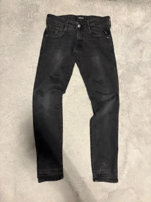 Replay Anbass svarta jeans - Svarta Replay Anbass jeans med snygg tvättad look och klassiska fem fickor. Jeansen har raka ben och diskreta sömmar på bakfickorna. Materialet är mjukt och stretchigt jeans, perfekt för en chill och stilren vibe.