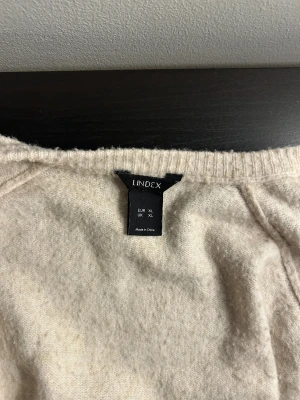 Beige kofta från Lindex XL - Mysig beige kofta från Lindex i storlek XL. Koftan har rund halsringning, långa ärmar och svarta knappar framtill. Materialet känns mjukt och stickat, perfekt för att hålla värmen under kyliga dagar. Enkel och clean design som funkar till många olika stilar.