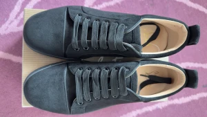 Christian Louboutin svarta sneakers - Svarta sneakers från Christian Louboutin med lyxig röd sula och signatur på undersidan. Skorna har rund tå, platt sula och snörning. Utsidan är i mocka med diskreta metalldetaljer på sidan och beige innersula. Perfekt för dig som gillar stilrena och exklusiva sneakers.