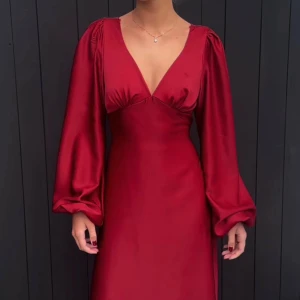 Röd långklänning i satin med v-ringning - Elegant röd långklänning i glansig satin med djup v-ringning och långa puffärmar. Klänningen har djur ringning i ryggen och knyt. Perfekt för jul eller bal!😊 Endast använd en gång!