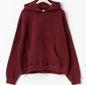 Vinröd hoodie med huva och ficka - Säljer en vinröd hoodie med stor magficka och huva. Tröjan har en loose passform och långa ärmar, perfekt för chill dagar. Materialet är mjukt och skönt, troligen bomull eller polyester. Enkel och stilren design utan mönster eller detaljer.