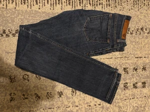 Mörkblå jeans från Skogsberg, 27/34 - Snygga mörkblå jeans från Skogsberg, modell gracious. Klassisk femficksdesign med bruna sömmar och läderpatch bak. Jeansen har rak passform och är tillverkade i slitstarkt denimtyg. Perfekt för dig som gillar tidlös stil och vill ha ett par jeans som funkar till allt.