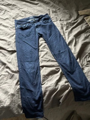 Mörkblå Armani Jeans straight fit - Snygga mörkblå jeans från Armani Jeans med klassisk femficksdesign och raka ben. Jeansen har diskreta sömmar, metallknapp med logga och patch bak. Materialet är mjukt denim som sitter skönt och ger en clean look.