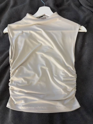 Beige polotopp från H&M i S - Säljer en beige polotopp från H&M i storlek S. Ärmlös topp och den går upp lite vid halsen