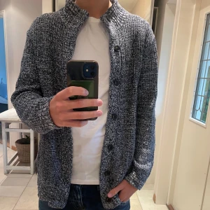 Stickad kofta navy M - Säljer en marinblå stickad kofta från Old Navy i storlek M. Koftan har huva, långa ärmar och knappar framtill. Materialet är mjukt och grovstickat, perfekt för kyliga dagar. Snyggt mönster med vita och grå toner som ger en cool vibe.