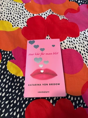 Hur kär får man bli? - En ungdomsroman om omöjlig och förbjuden kärlek, där huvudpersonen ställs inför svåra val mellan vänskap och känslor. Perfekt för dig som gillar romantik, konflikter och starka känslor. Modern, rosa omslag med hjärtan och läppar gör boken extra attraktiv för unga.