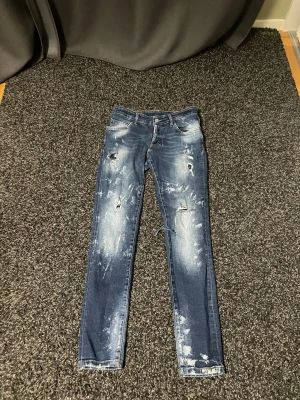 Dsquared2 blå skinny jeans, stl 42 - Snygga blå jeans från Dsquared2 i storlek 42 med slitna detaljer och blekta partier för en cool, edgy look. Modellen är skinny med normal passform och klassisk femficksdesign. Materialet är jeans med dragkedja och knapp framtill.