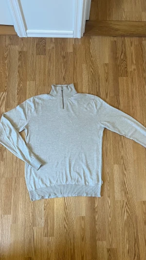 Ljusgrå polotröja från Jack & Jones - Snygg ljusgrå polotröja från Jack & Jones med half zip-dragkedja i halsen. Tröjan har långärmad design och är tillverkad i mjuk bomull, perfekt för dig som gillar stilrena och enkla plagg. Ribbad mudd vid ärmslut och nederkant för extra komfort.