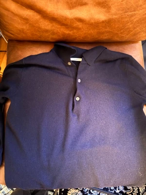 Marinblå merinoull pikétröja A Day's March - Snygg marinblå merinoull pikétröja från A Day's March i storlek M. Tröjan har klassisk krage, tre knappar framtill och långärmad design. Perfekt för dig som gillar stilrena och tidlösa plagg med en modern touch.