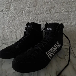 Svarta Lonsdale boxningsskor - Säljer ett par svarta Lonsdale boxningsskor med högt skaft och snörning. Skorna har meshpaneler för extra ventilation och detaljer i syntetmaterial. Pris kan diskuteras 