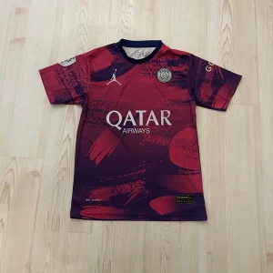 PSG Mbappé fotbollströja Jordan x Nike - Snygg PSG fotbollströja med Mbappé 7 på ryggen, tillverkad i lätt och ventilerande material. Tröjan har en cool mix av röd och mörkblå färg med abstrakt mönster, Paris Saint-Germain-märke på bröstet och Jordan-logga. Perfekt för dig som älskar fotboll och streetstyle.