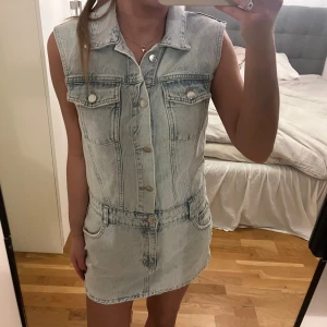 Ärmlös jeansklänning från Pull&Bear - Snygg ljusblå ärmlös jeansklänning från Pull&Bear med klassisk krage, knappar framtill och fickor både fram och bak. Skulle säga att den är ganska liten i storleken!