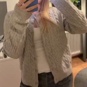 Grå stickad kofta - Mysig grå kofta med kabelstickat mönster och rund hals.