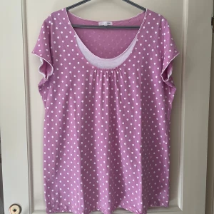 Rosa prickig topp från Ellos strl 54/56 - Söt rosa topp från Ellos med vita prickar och rund halsringning. Modellen är kortärmad och har en lös passform som känns chill och bekväm. Tillverkad i 100% bomull. Storlek 54/56.