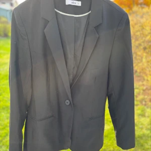 Svart kavaj från Ellos, storlek 46 - Klassisk svart kavaj från Ellos i storlek 46. Enkelknäppt modell med två fickor framtill och snyggt skräddad passform. Perfekt för en stilren look och funkar lika bra till skjorta som t-shirt.