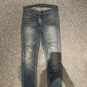 Blå  jeans från Lee W28 L32 slim fit - Snygga blå jeans från Lee i modellen slim med klassisk femficksdesign och diskret slitning framtill. Jeansen har normal midja och raka bakfickor med Lee-logga. Perfekta för dig som gillar en smal passform och stilren look. Bara  skriva ifall ni har frågor!