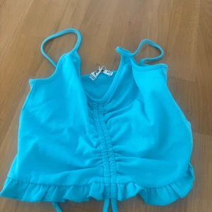 Turkos linnetopp med volang från Pull&Bear - Säljer en turkos linnetopp från Pull&Bear med smala axelband, rynkad detalj framtill och volangkant nedtill. Toppen är croppad och har en snygg dragsko i mitten. Perfekt för sommarens alla tillfällen!