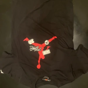 Jordan svart t-shirt med röd logga - Svart t-shirt från Jordan med stor röd Jumpman-logga och texten 'Flight', 'AIR' och siffran 23 på bröstet. Skön passform och tillverkad i en mix av bomull och polyester. Perfekt för dig som gillar sportig streetstyle.