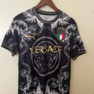 Svart fotbollströja - Unik svart fotbollströja med guldiga detaljer, Italiens landslagsemblem och pampigt barockmönster i vitt och grått. Kortärmad modell med klassisk rund hals och dekorativa gulddetaljer på krage och ärmslut. Perfekt för dig som vill sticka ut på planen.