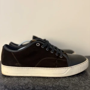 Lanvin Skor - Snygga svarta sneakers med ovandel i mjuk mocka och tåparti i slätt skinn. Skorna har svarta snören, silverfärgade öljetter och en vit platt sula som ger en clean look. Perfekta för dig som gillar stilrena och klassiska sneakers med en twist.
