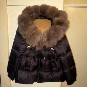 Svart pufferjacka med stor pälskrage - Säljer en svart pufferjacka med en riktigt stor och fluffig brun pälskrage. Jackan har dragkedja, snörning i midjan och stora fickor framtill. Helt ny oanvänd i storlek M