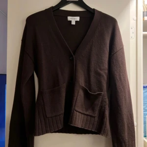 Brun stickad kofta med fickor - Mysig brun stickad kofta från & other stories med v-ringning, stora knappar och två rejäla fickor framtill. Koftan har långa ärmar med bred ribbad kant och en avslappnad passform. Perfekt att slänga på sig när det är kyligt ute. Nypris 990kr och är helt ny