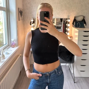 Svart ribbad croppad topp med öppen rygg - Säljer en svart croppad topp i ribbad bomull med ärmlös design ifrån Zara. Toppen har en snygg öppen rygg med knytband som ger en cool detalj. Använd endast 1 gång