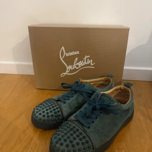 Mörkgröna Christian Louboutin sneakers - Unika mörkgröna sneakers från Christian Louboutin i mocka med coola nitar på tån och klassisk röd sula. Skorna har snörning och rund tå, samt exklusiva detaljer som sticker ut. Perfekta för dig som vill ha något extra och vågar sticka ut. Passar storlek 40 till 41,5