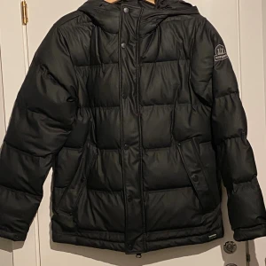 Svart baffle jacka från Tretorn!  - Svart baffle från Tretorn med huva och dragkedja framtill. Superfin svart Tretorn Buffle jacka!  Innerficka Dragkedja  Luva ( fast)  2 fickor fram med knappar  Färgen är mattare är på bilden.  Mycket bra och fint skick. Använd max 10 gånger. Så är i nyskick!   