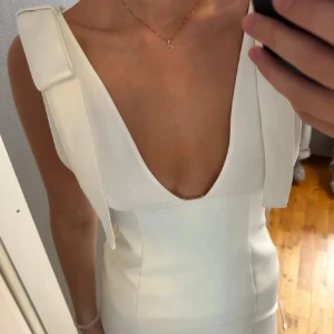 Vit kortklänning med djup v-ringning - Säljer en stilren vit kortklänning med djup v-ringning och breda axelband. Klänningen har en figurnära passform och är perfekt för dig som vill sticka ut. Materialet känns slätt och har en snygg struktur. Passar till många olika tillfällen!